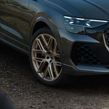 Close-up of Audi RS Q8 front wheel on gravel road.