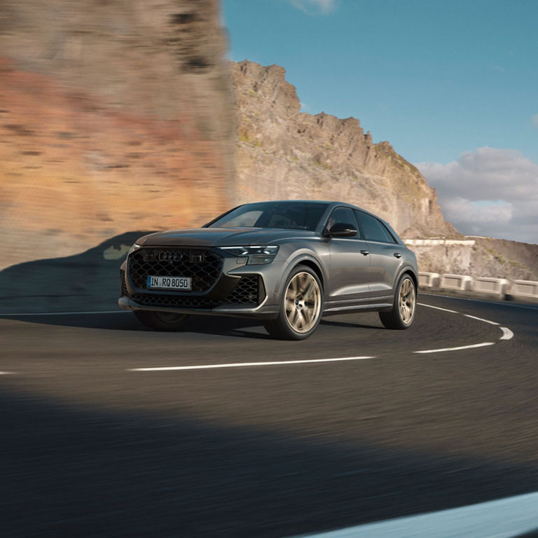 Dark grey Audi RS Q8 turning into a bend driving up a mountainside road.