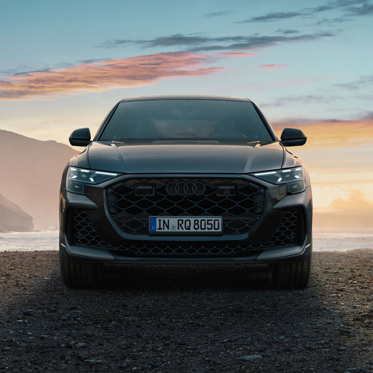 Front view of a parked Audi RS Q8 on a rocky road with a mountain range in the background.