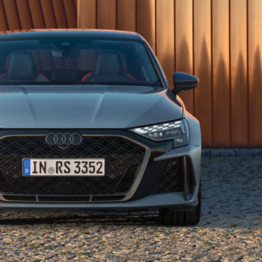 A grey Audi RS3 Saloon vehicle parked in front of an orange wall, partial front view shown.
