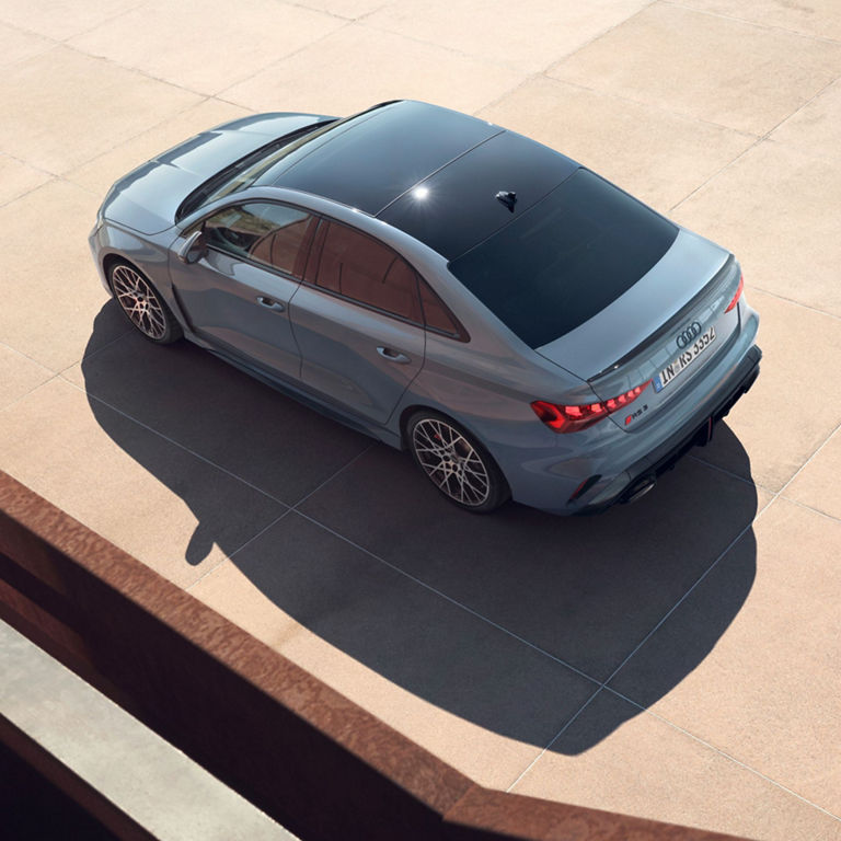 Aerial view of a modern grey Audi RS3 Saloon parked on a concrete surface.