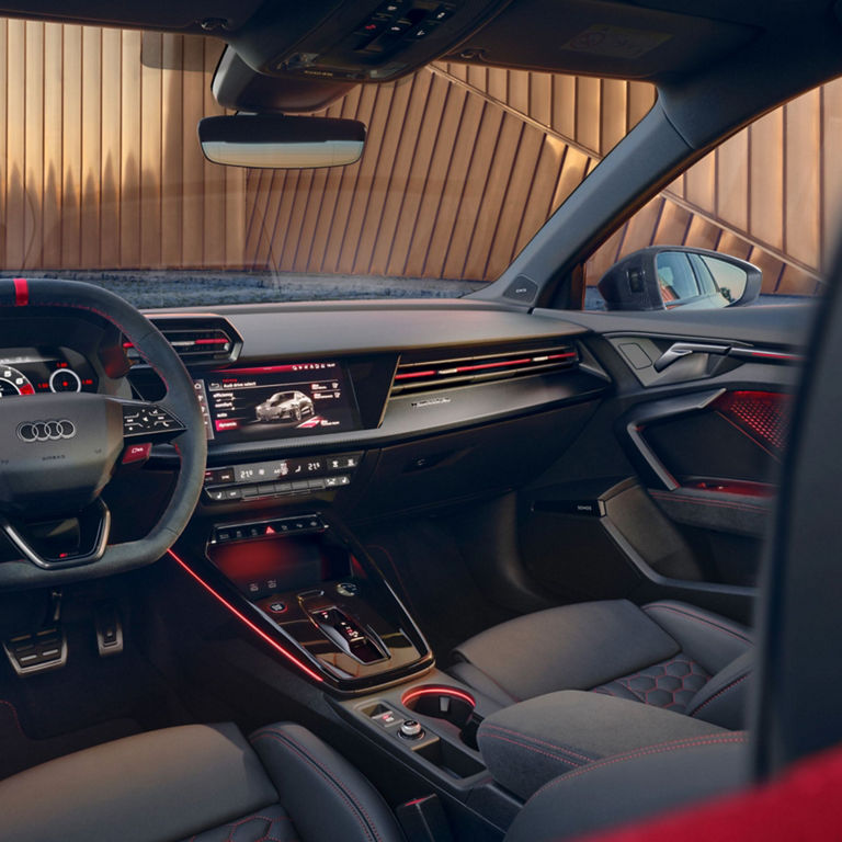 Interior of a modern Audi RS3 car with a touchscreen dashboard display and red ambient lighting.