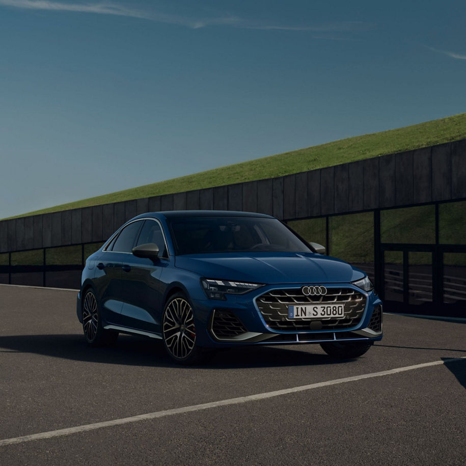 Blue Audi RS3 Saloon parked on pavement with grassy backdrop.