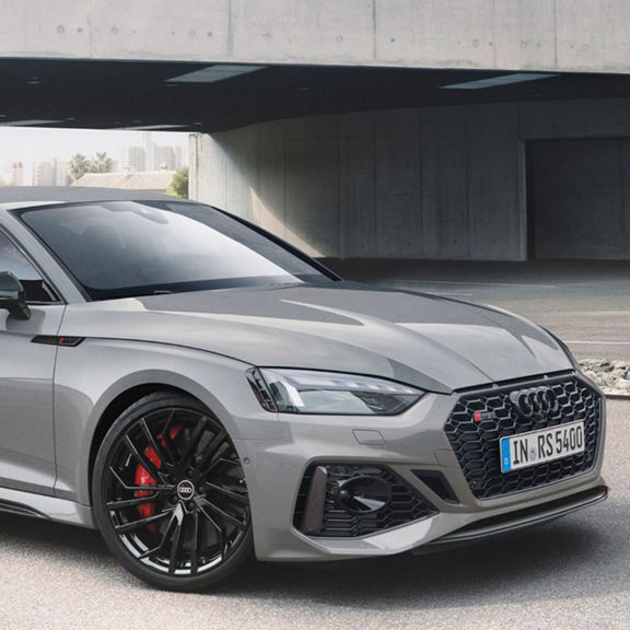 Person in a white suit standing next to a grey coupe.