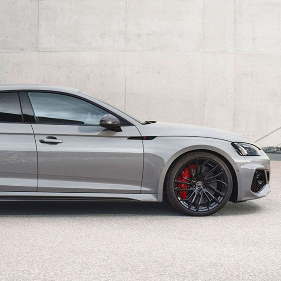 A silver RS5 Sportback with black rims and red brake callipers parked outside a building.
