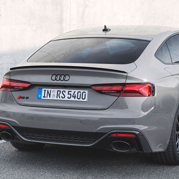 Rear view of a parked Audi RS5 Sportback in grey, near a concrete wall.