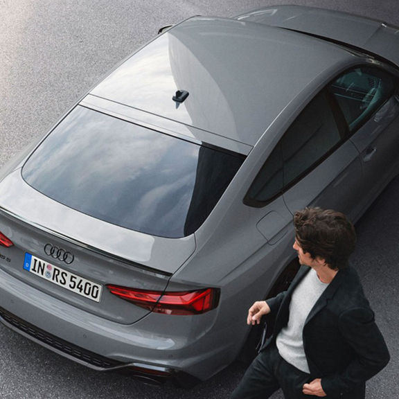 Two people standing beside a parked grey Audi RS5 Sportback.