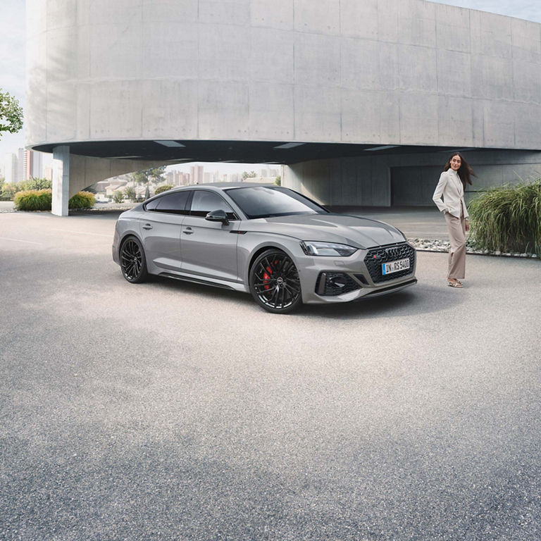 A grey Audi RS5 Sportback car parked outside a building with a person standing beside it.