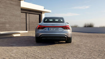 Silver Audi S-e-tron GT parked outside a modern house with a clear sky.