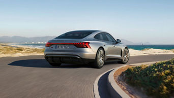 A silver Audi S-e-tron GT driving along a coastal road with mountains in the distance.