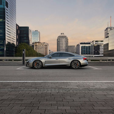 Electric Audi car charging at a station in urban parking area at dusk.