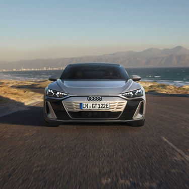 A silver Audi S-e-tron GT driving on a coastal road with mountains in the background.