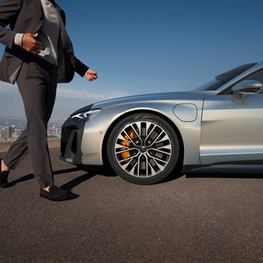 Man in a suit walking towards a silver car with city skyline in the background.