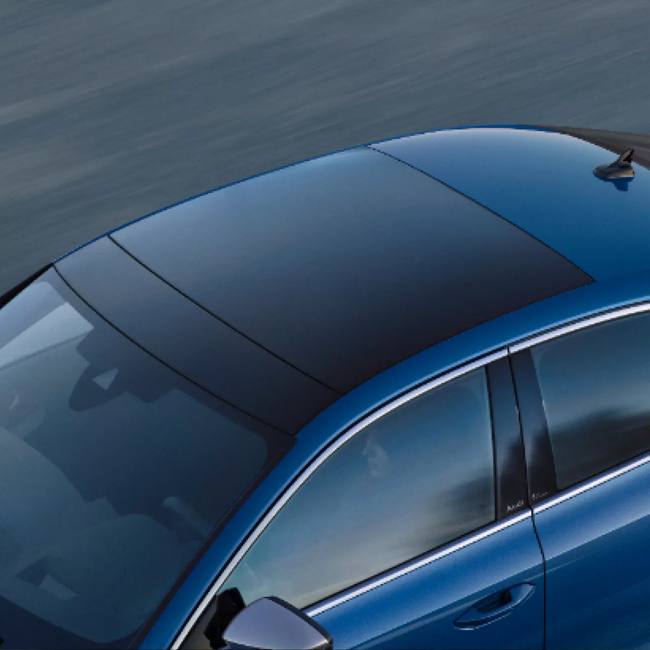 A blue car in motion seen from a top side angle, highlighting the sunroof.