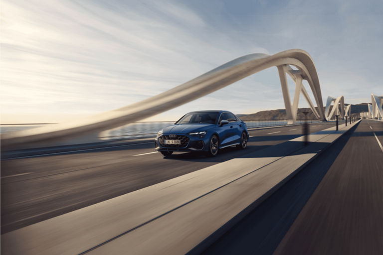 A blue car driving on a bridge with a unique arch structure under a clear sky.