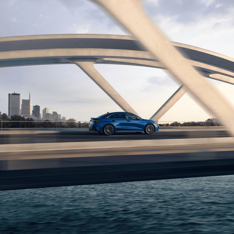 Blue car speeding over a bridge with modern city skyline in the background.