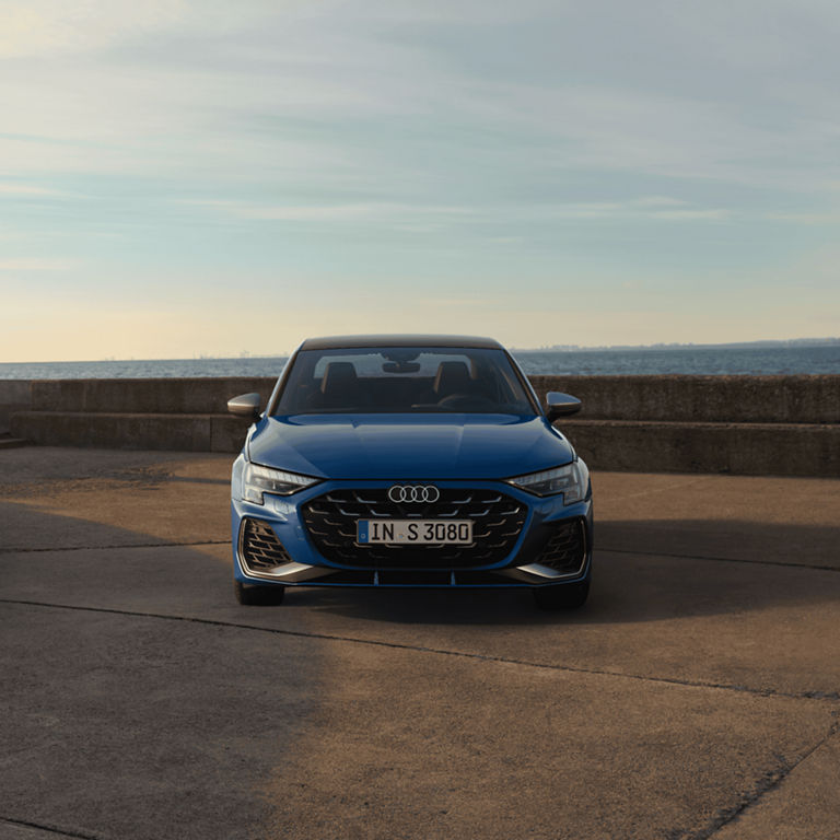 Blue Audi car parked on a road by the sea.