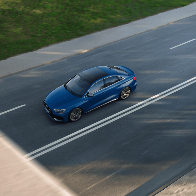 Aerial view of a blue Audi car driving on a road with motion blur effect.