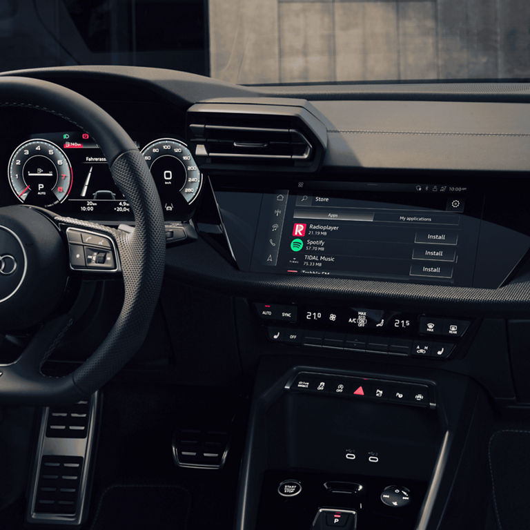 An Audi car interior with steering wheel, dashboard display, and center console touchscreen controls.