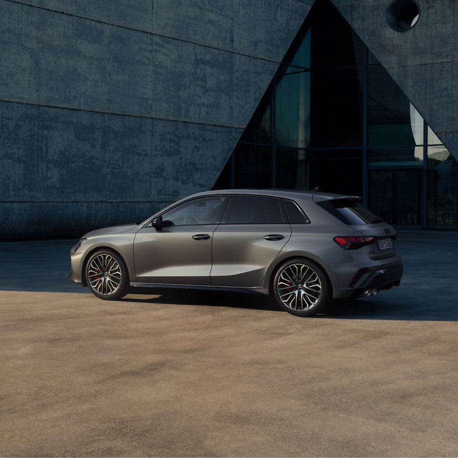 An Audi S3 Sportback car parked beside a building with large glass windows and a concrete exterior.