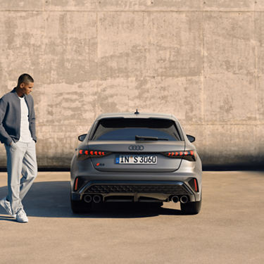  A person standing next to a parked Audi S3 in front of a concrete wall.