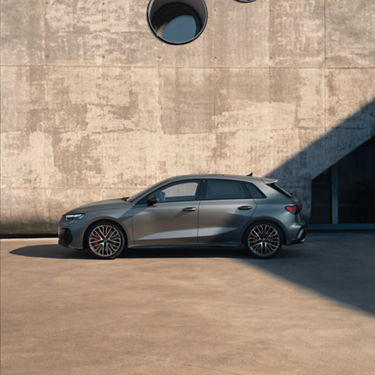  A modern grey Audi S3 car parked by a concrete building with circular windows.