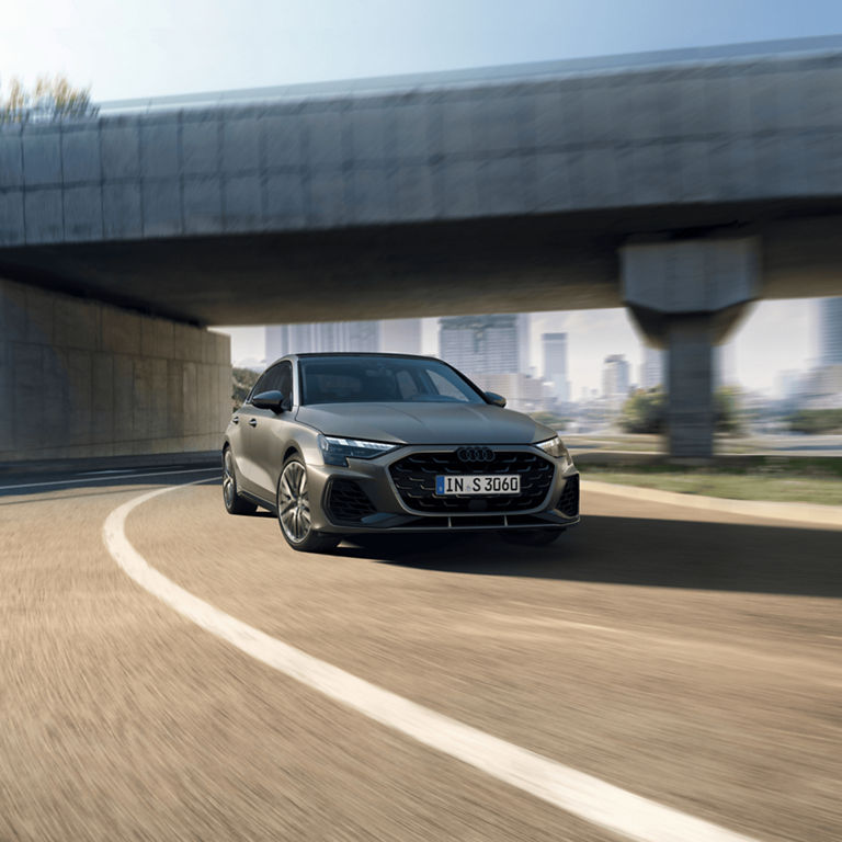 Audi S3 Sportback car driving under an overpass on a sunny day with blurred background indicating motion.