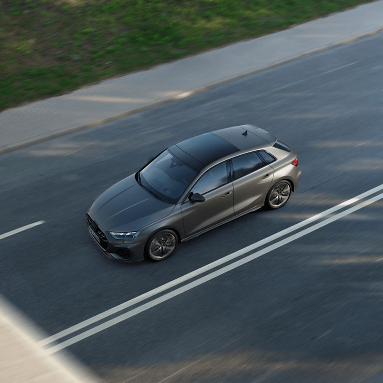 Aerial view of a grey Audi S3 Sportback car driving on a sunlit road.