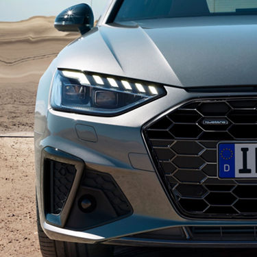 Close-up of a silver car's front end with LED headlights and a hexagonal grille, against a desert backdrop.