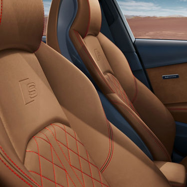 Car interior with brown leather seats featuring red stitching.