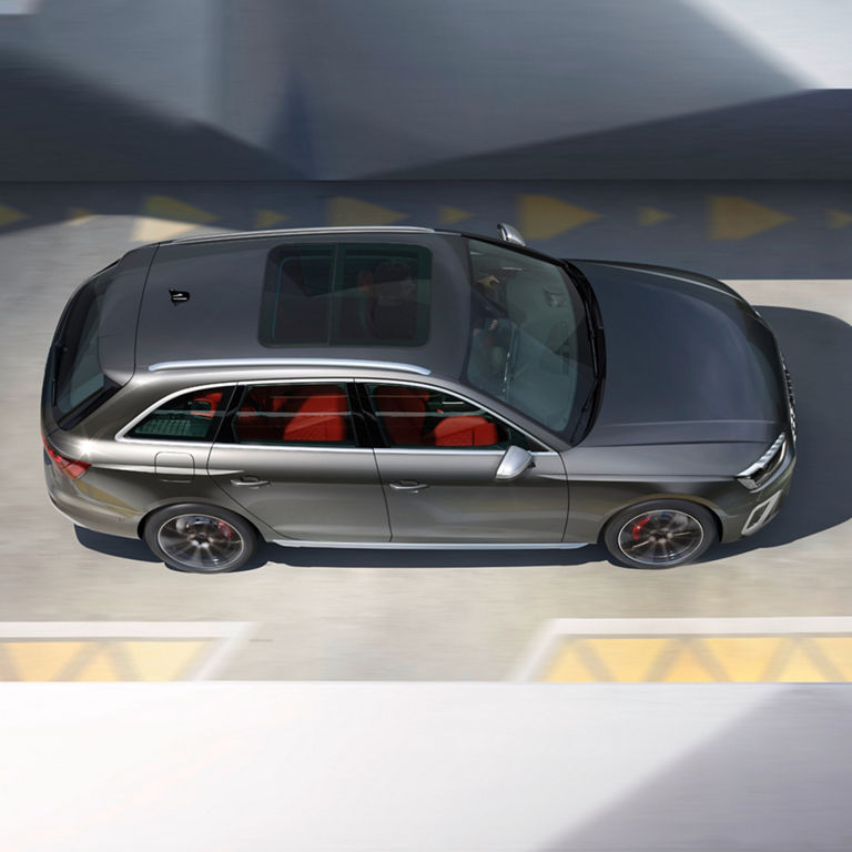 Aerial view of a silver car driving over a shadow-cast road with visible yellow markings.