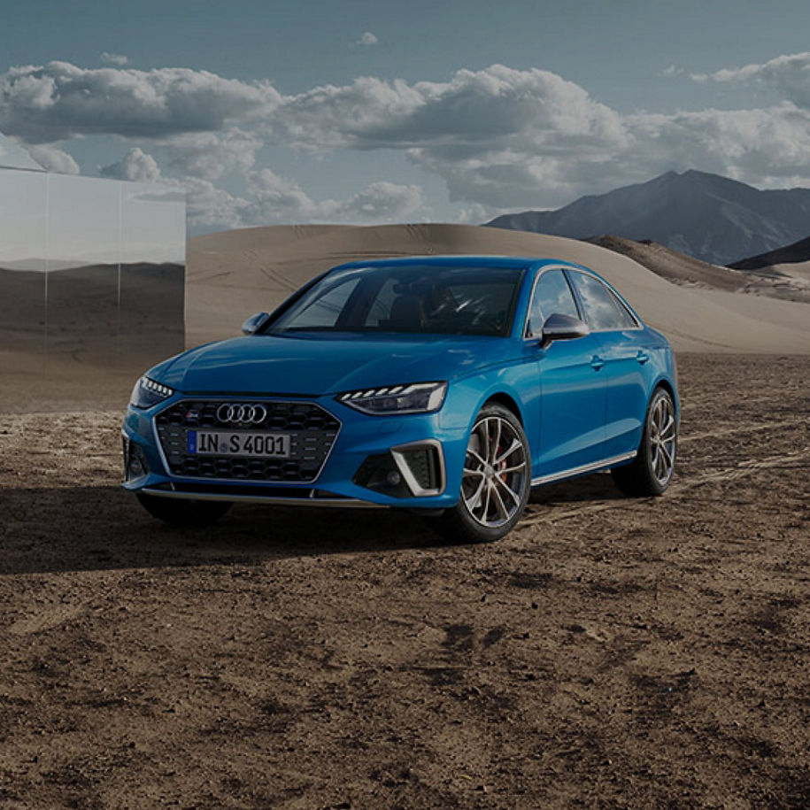 Blue sedan in desert landscape under cloudy sky.