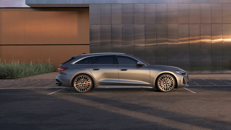 A silver Audi S5 Avant parked outside a building with a metallic facade during sunset.