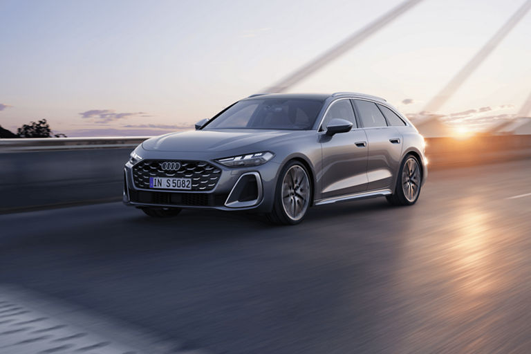 A silver Audi S5 Avant car driving on a road at dusk, with sun setting in the background.