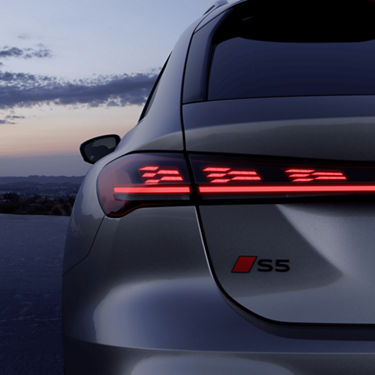 Rear view of a grey Audi S5 Avant car with distinctive taillights on at dusk.