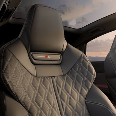 Car's seat with diamond stitching and a sunset view through the window.