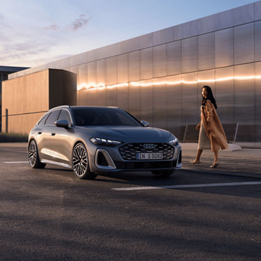 A silver Audi parked outside a modern building at sunset. 