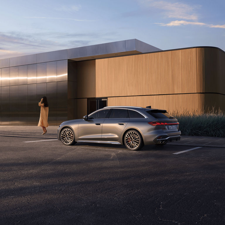 Audi car parked outside a modern building at sunset with a person walking by.