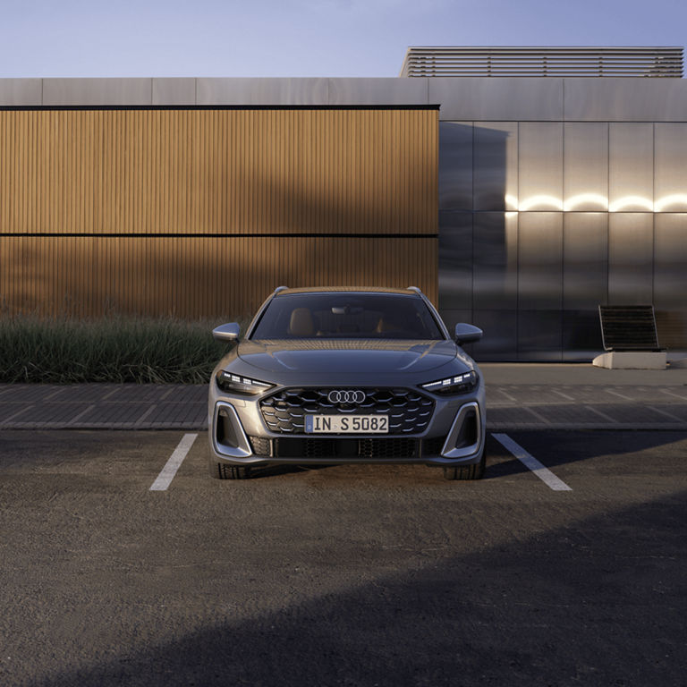 A silver Audi parked in front of a modern building at dusk.