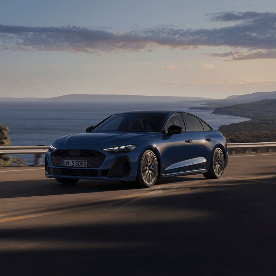 Blue Audi driving along a coastal road at dusk.