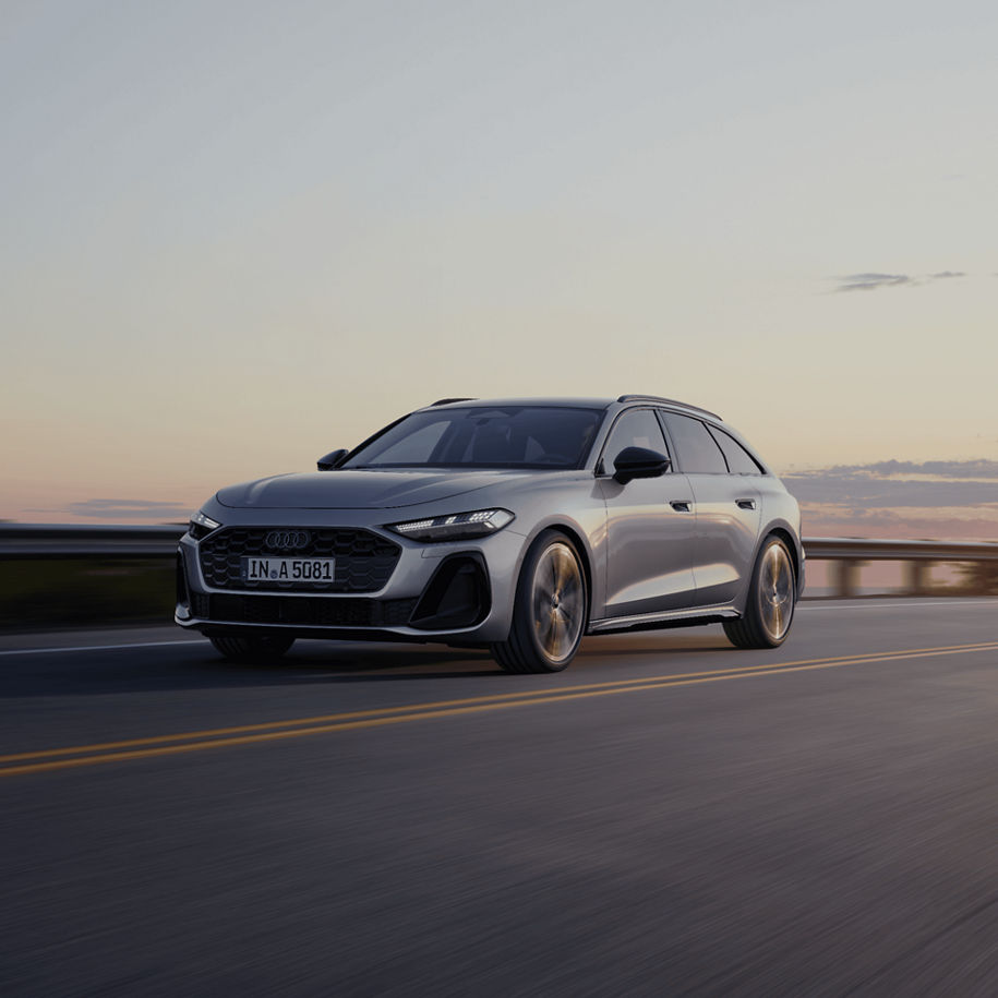 A silver Audi driving on a road at dusk.