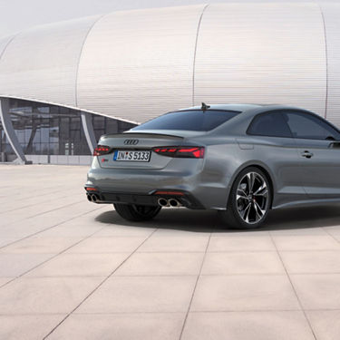 Rear view of a grey Audi car parked by a modern building.