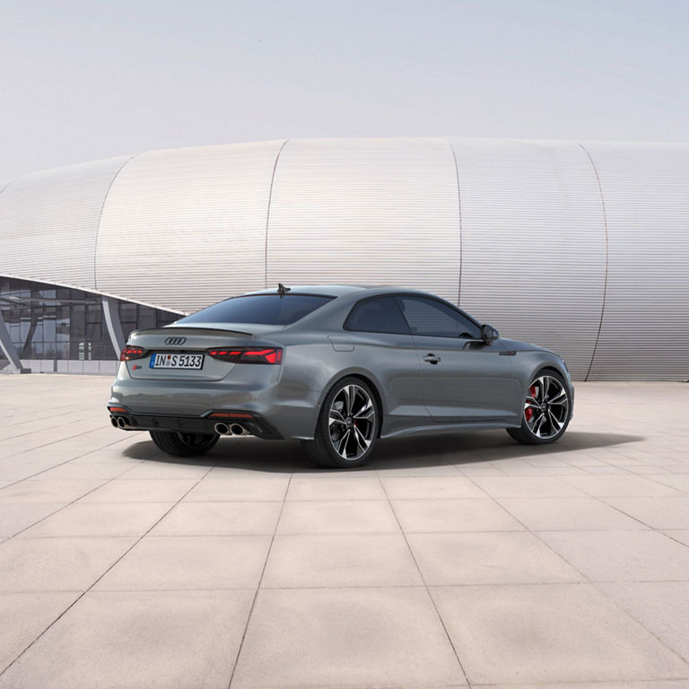 A grey Audi coupe parked outside a modern building.