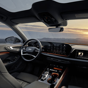 Interior view of an Audi car with dashboard and steering wheel, sunset outside.