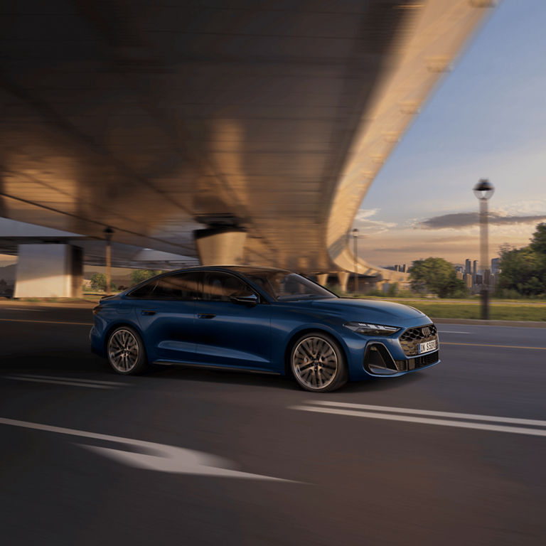 Audi S5 Saloon driving under a bridge at dusk, showcasing speed with motion blur.