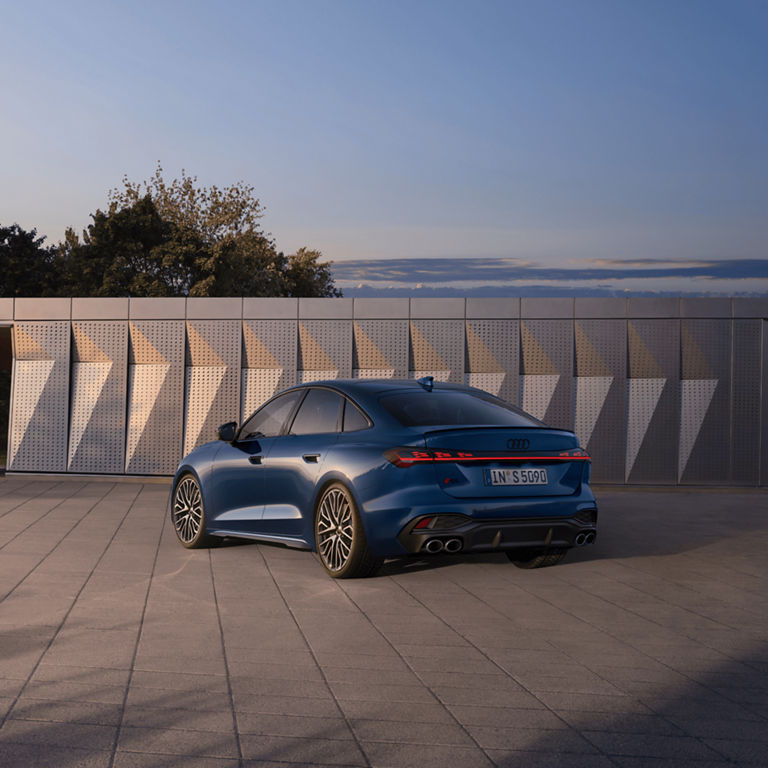 A blue Audi S5 Saloon parked near a modern building at dusk.