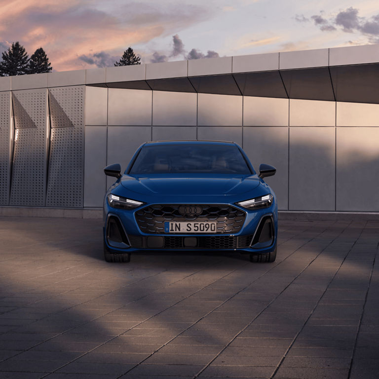 Blue Audi car parked in front of a modern building at dusk.