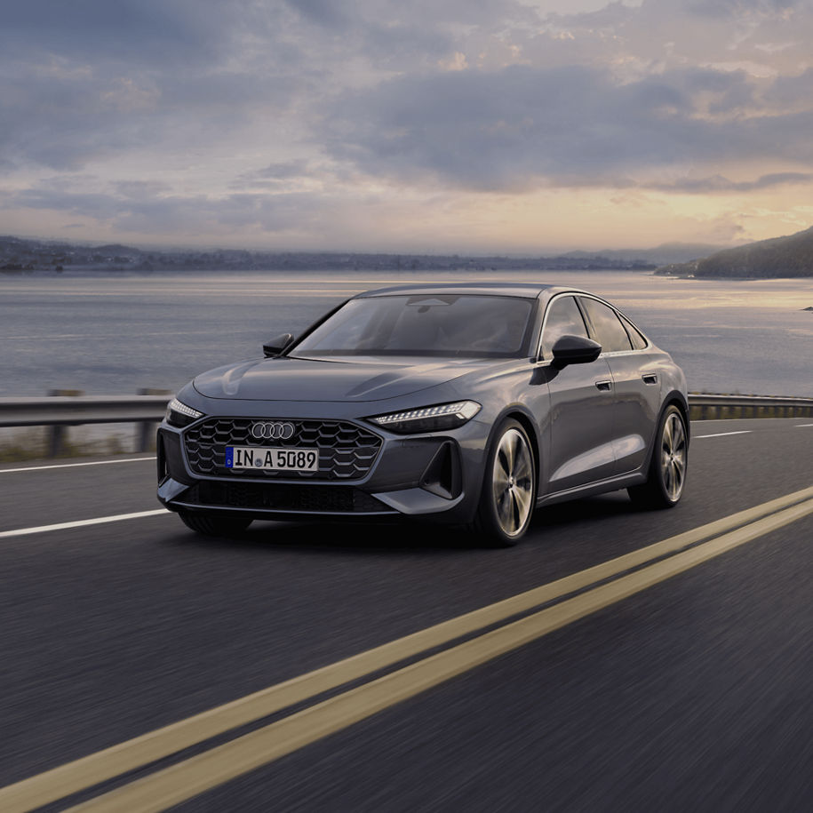 A grey Audi sedan driving along a coastal road at dusk.