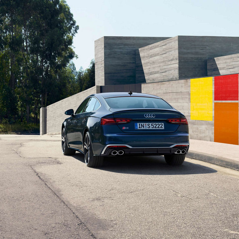 A blue Audi S5 Sportback parked on the street with colorful geometric wall art in the background.