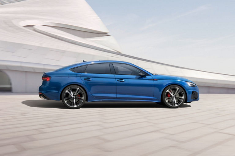 A blue Audi S5 Sportback driving past a modern white building with a sleek design.
